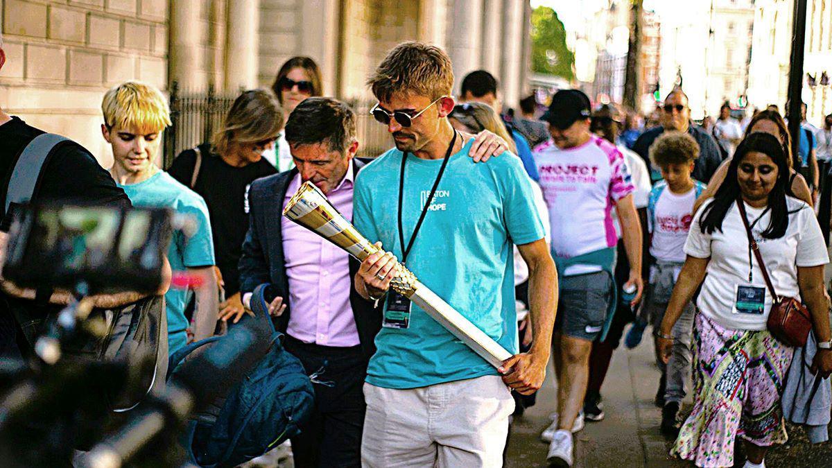 A man holding the Baton of Hope during an event in Kent in 2023 with another man putting his arm around him and others in the background
