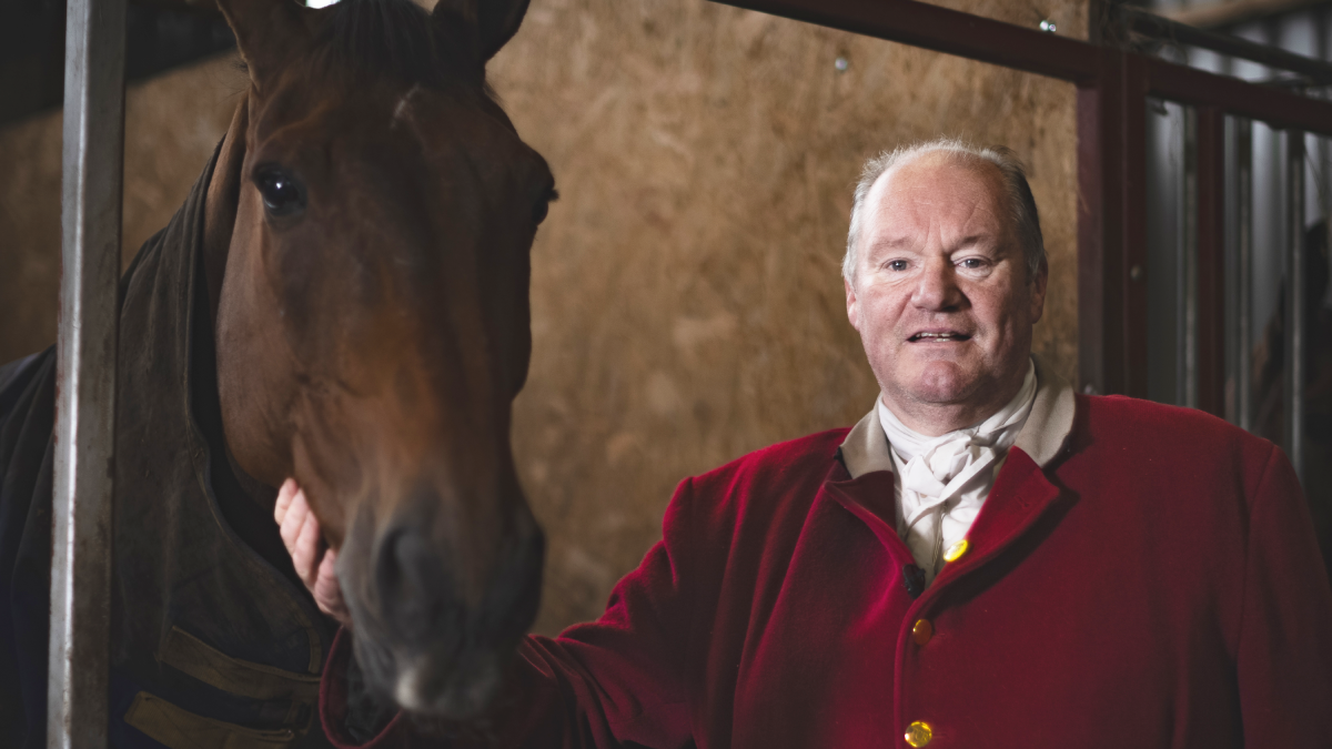 Huntsman Byron John in red jacket looks at the camera, while patting his horse