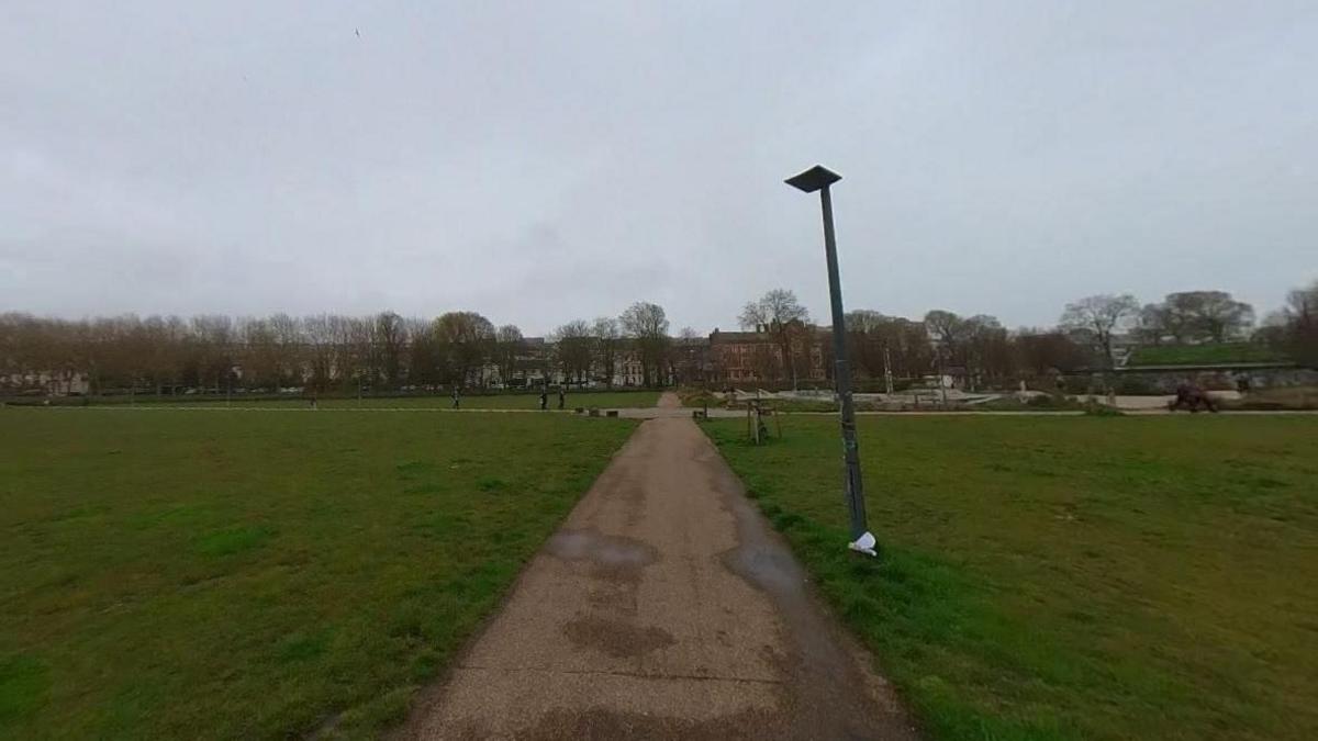 A large green open space with a central pathway. Trees are in the background