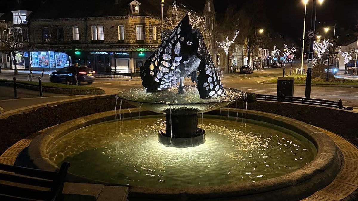 A fountain made from steel with water flowing through it, lit up from below 