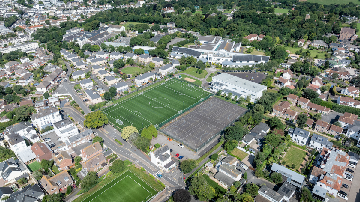 Aerial view of housing estates surrounding a football pitch, grey pitch and school sports building