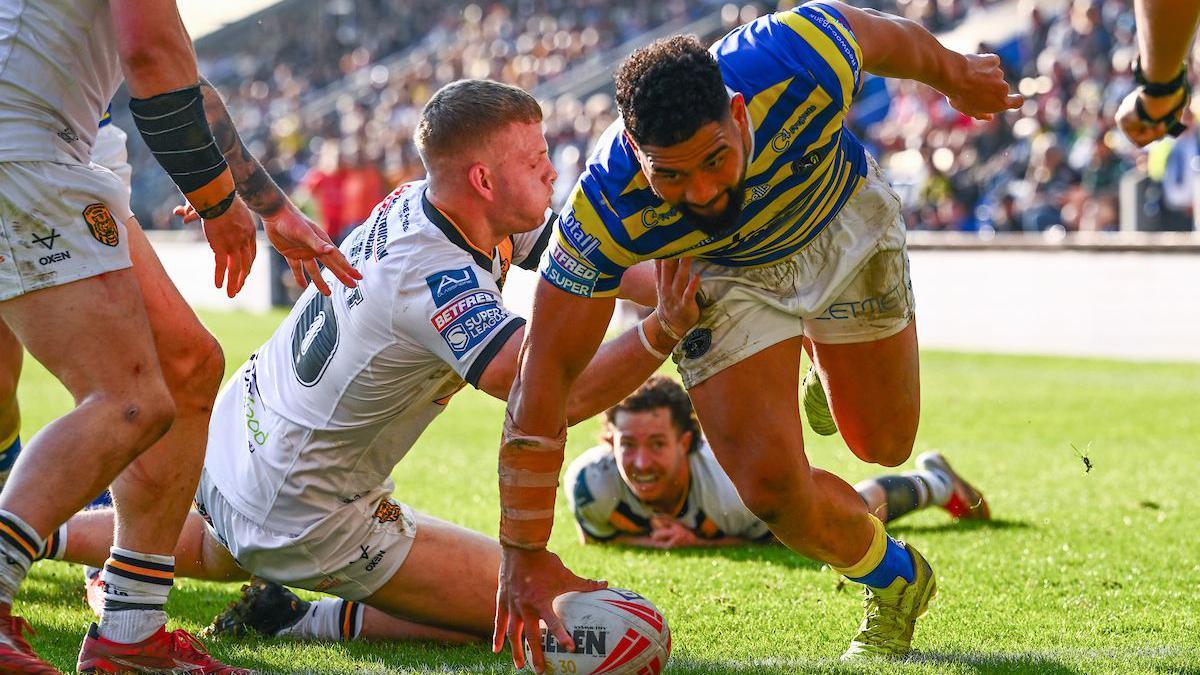 Warrington forward Kelepi Tanginoa, in primrose and blue, touches down the ball for his hat-trick try as a Castleford player in all-white tries to stop him and two more look on.