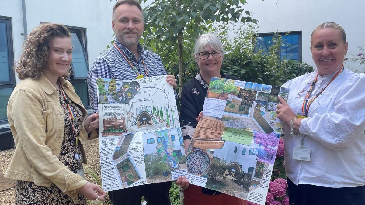 Four membrs of staff stand in a line, holding up plans for the garden