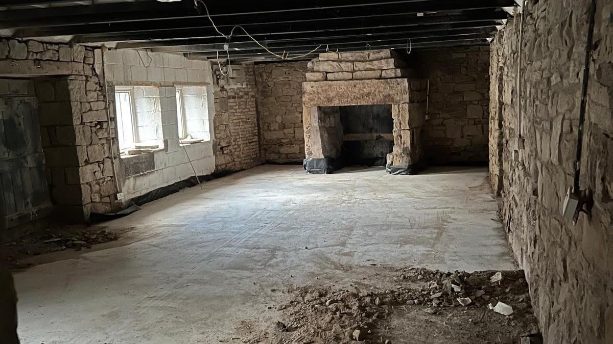 The interior of a pub during renovations showing an empty room with brickwork exposed and lots of dirt on the floor and wires hanging from the ceiling 