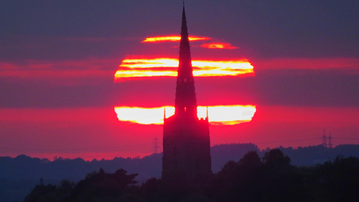 A church spire silhouetted against a red sun 