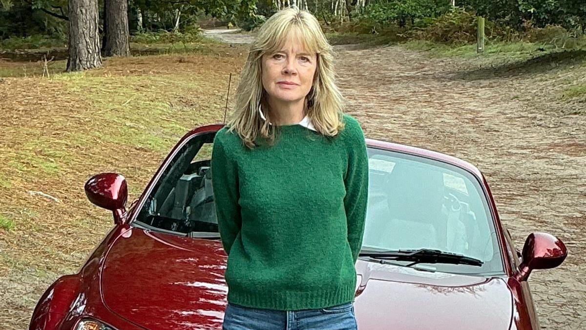 Glynis Jenkin's is stood in the middle of the image sat on the bonnet of her red Mazda MX-5. She had shoulder length blonde hair and was wearing a green jumper and blue jeans.