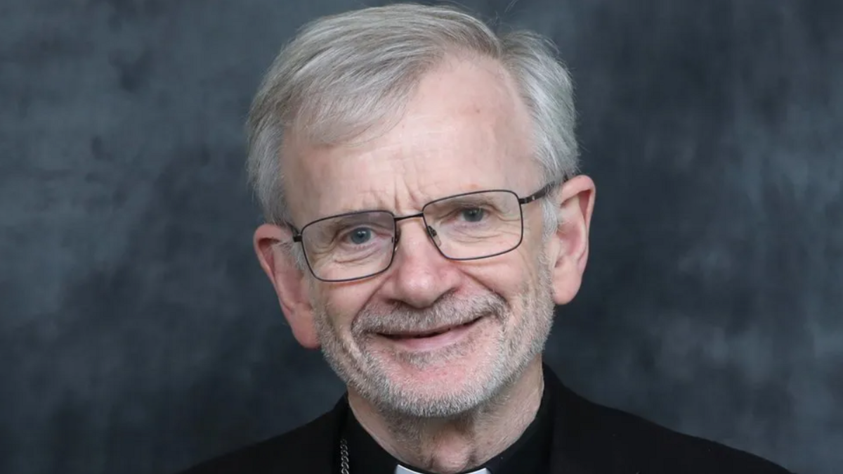 Man in glasses smiling into camera agaisnt a grey background