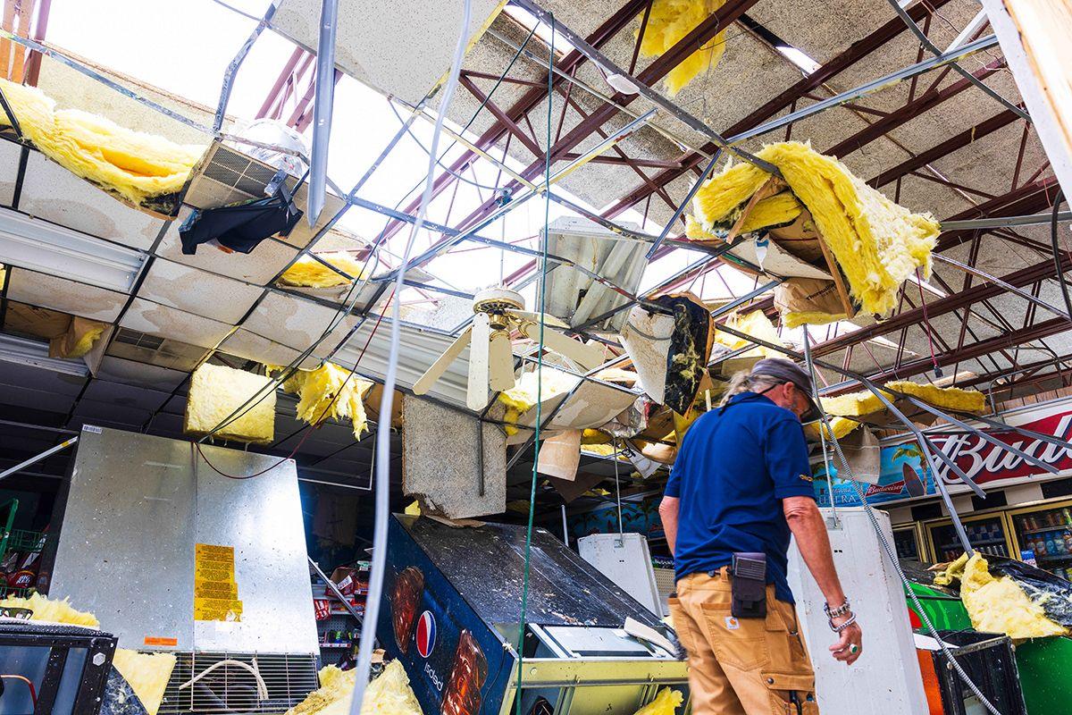 A man in a cap and wearing blue polo shirt surveys damage to a building missing many of its roof panels in St Lucie, Florida on 10 October