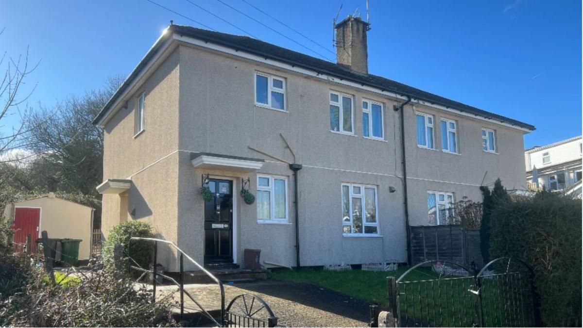 A property on Cobhorn Drive in Bristol. The flat is beige in colour with several windows on the front. The front door is black and to the side. There are hanging baskets either side of the door.