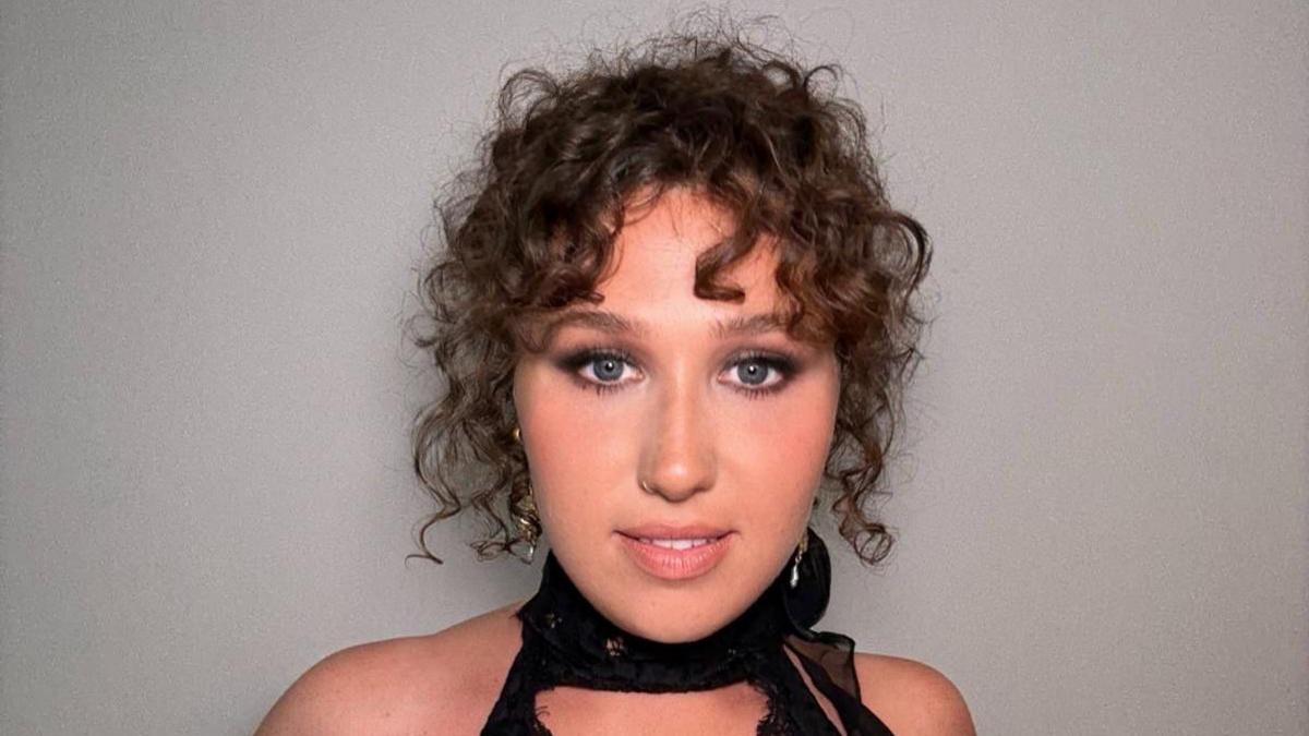 A girl with brown curly hair, put up into a classy messy bun, she's in a black halter neck dress, dressed for a special occasion. She is wearing makeup with smokey eye shadow and pink lips. Her eyes are a dark blue which makes the eyeshadow pop.