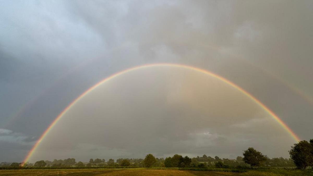 A rainbow in the sky over fields with the colours and rays of the rainbow all clearly visible.