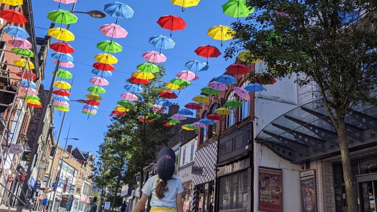 A child looking up at a number of colourful umbrellas in Stoke-on-Trent