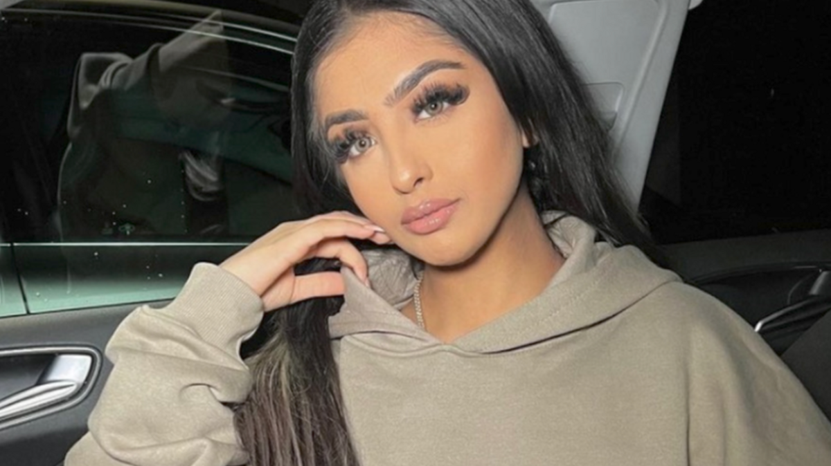 Woman with long brown hair in a car wearing a hoodie.