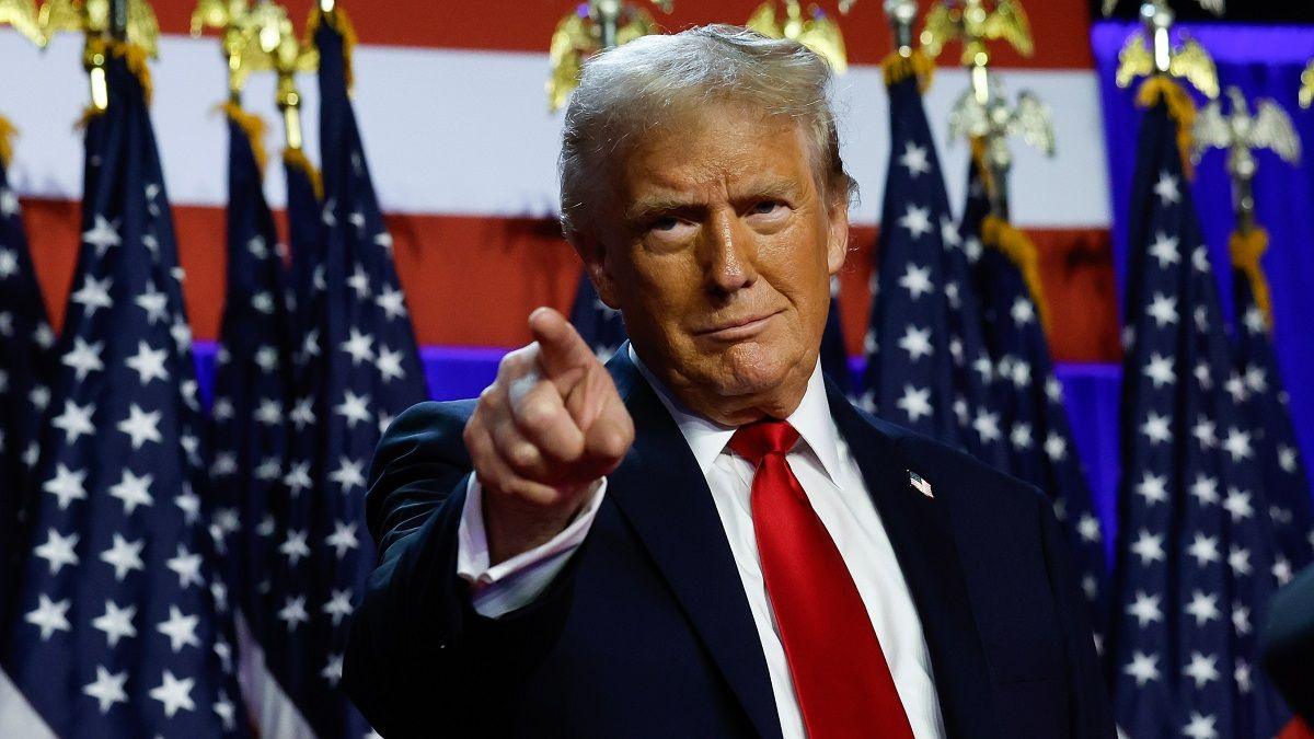 Donald Trump points as he stands in front of American flags on stage