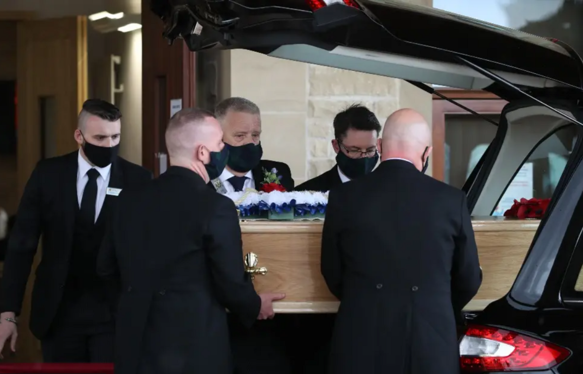 Five pallbearers take a coffin from a hearse at a funeral service