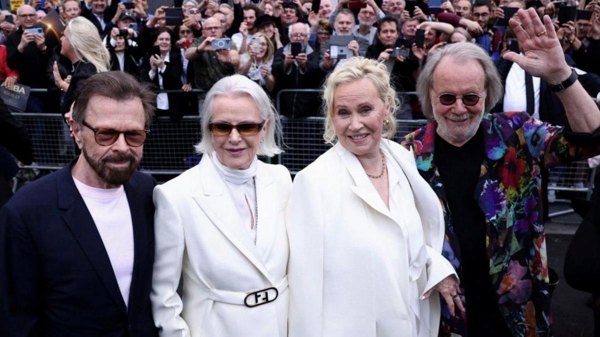 Abba from left: Björn Ulvaeus with dark brown hair and beard, shaded glasses wearing white T-shirt and dark blue jacket; Anni-Frid Lyngstad has white shoulder length hair, sunglasses, a white polo neck sweater and white coat, Agnetha Faltskog has a white suit with white blouse and short blonde hair; Benny Anderssson has long greying hair, a grey beard, sunglasses, a black polo shirt and long multi-coloured coat.