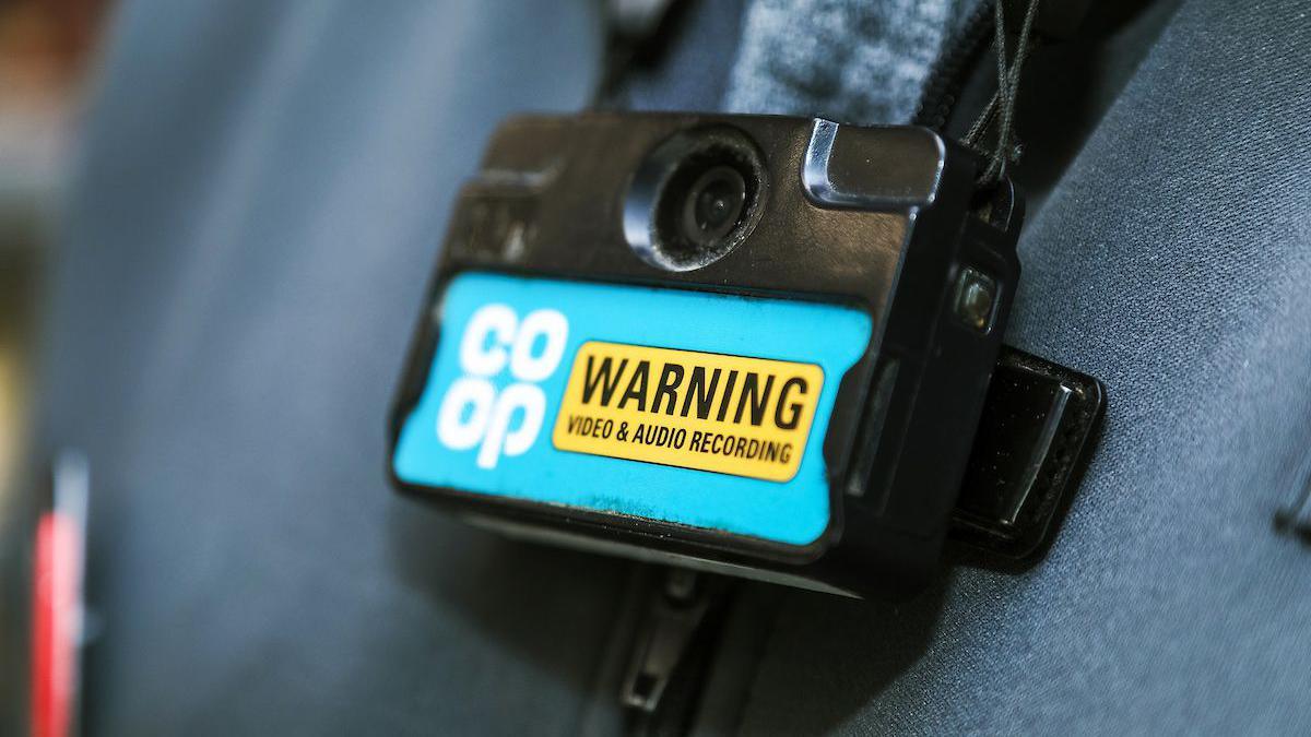 A body-camera on a Co-op staff member. The camera has a Co-op logo and a warning sign to show that people are being 'audio & video' recorded.