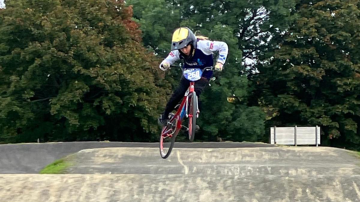 A girl on a BMX bike in mid-air - she is riding over one of the hills on the course.