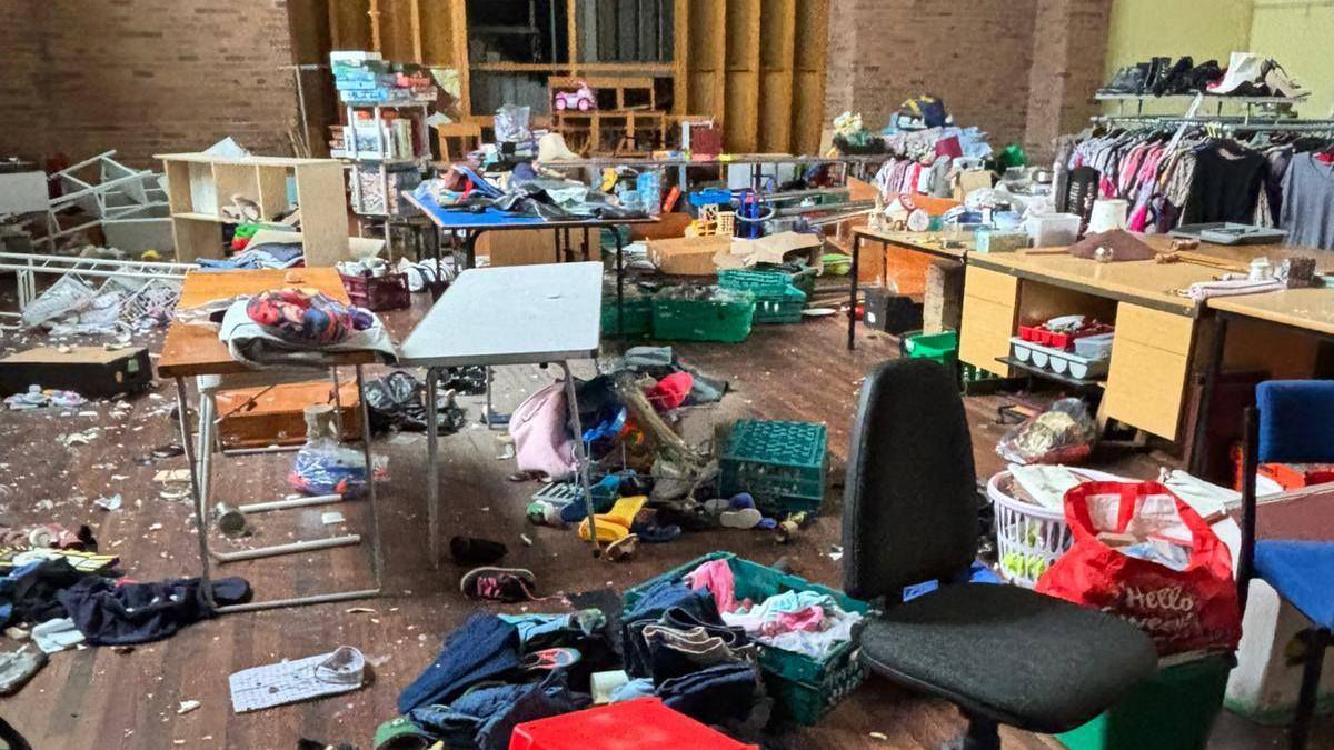 A room with tables that had been set out for a jumble sale seen with detritus, clothing, pots and shattered glass strewn across the floor.