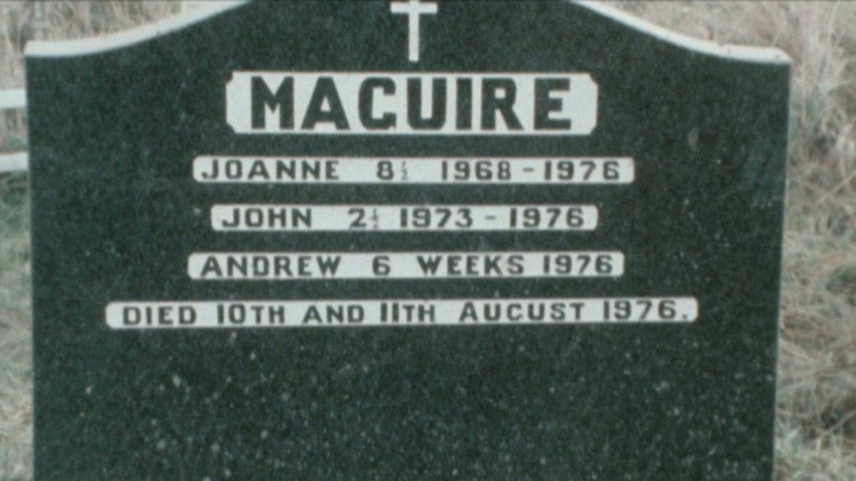 A gravestone with the nhame 'MAGUIRE' engraved in black capital letter into a surrounding block of white. The names 'JOANNE', 'JOHN' AND 'ANDREW' are also engraved in a similar way. At the top is a cross and beyond the white is granite. 