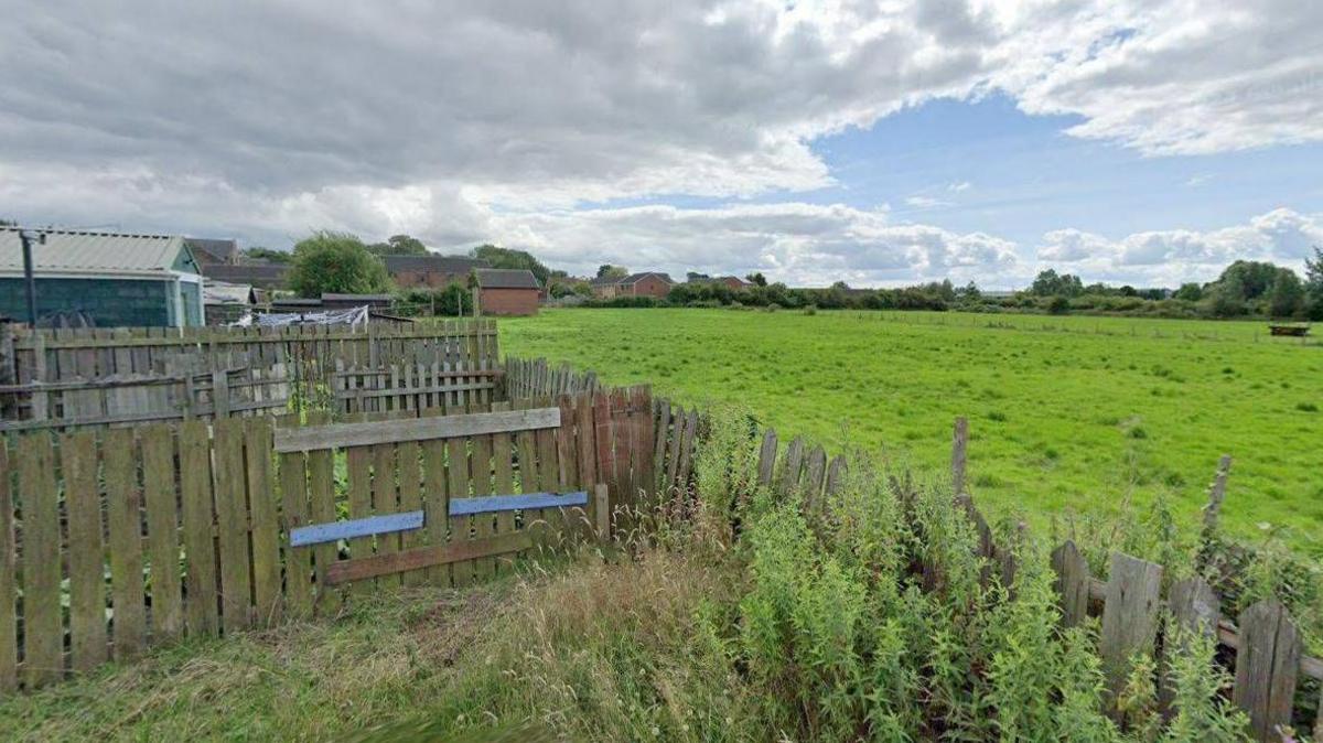 A Google Street View screengrab of the land where the homes would be built at Grange Farm. The site is a grassed area bordered by housing estates.