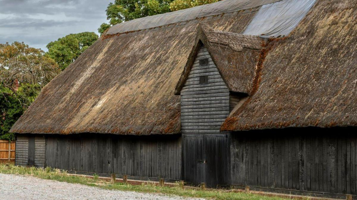 An exterior view of the barn and its decaying thatch roof