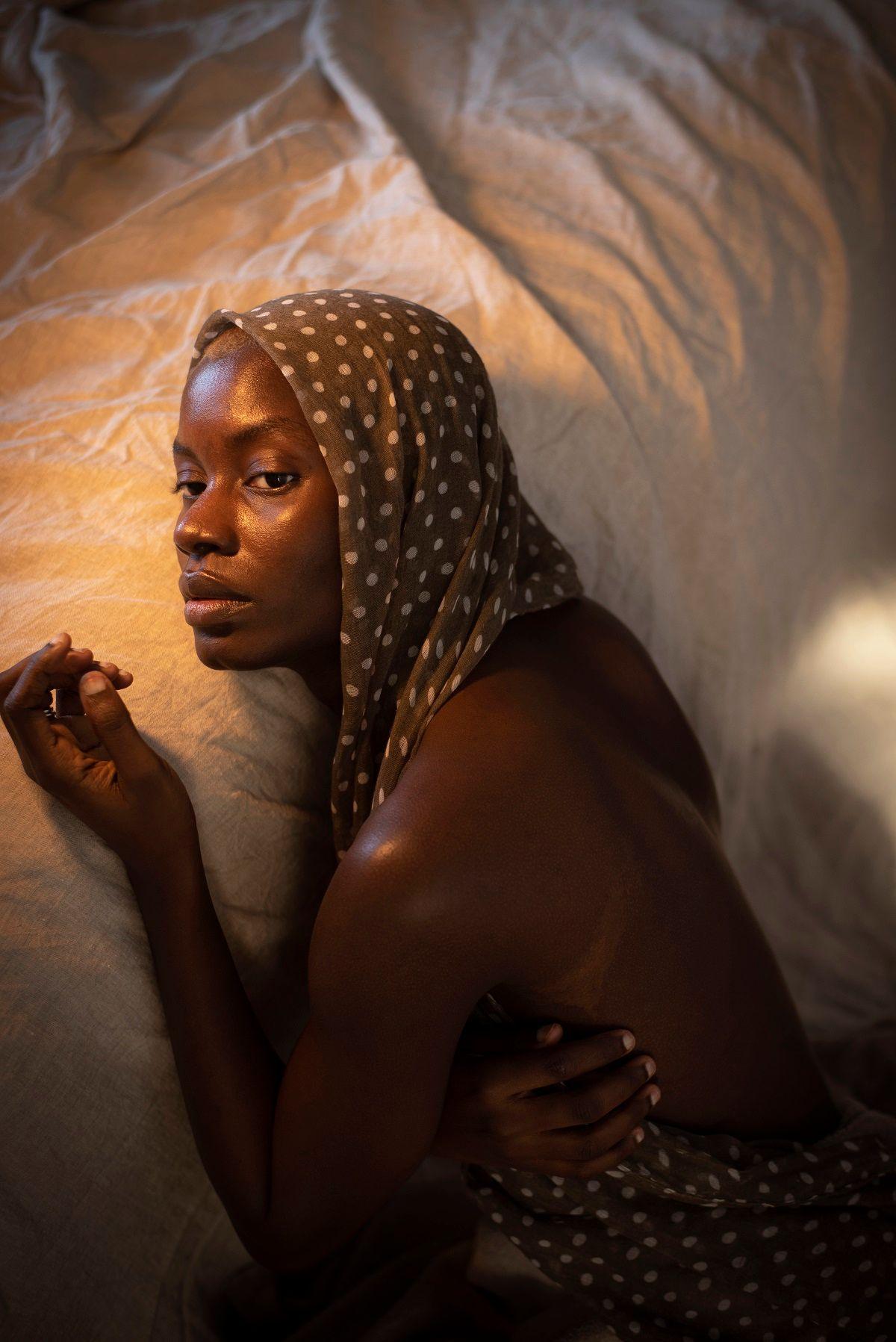 A wan-looking Dola Posh is lying on her bed with a green head covering with white spots. Her face is lit by a golden light.  