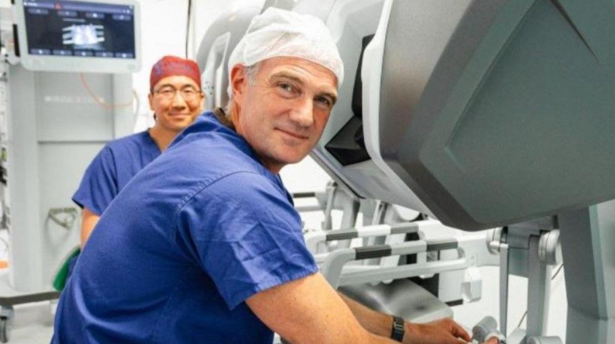 Peter Kyle is in the foreground wearing a health uniform and sitting next to equipment. David Mak is in the background.