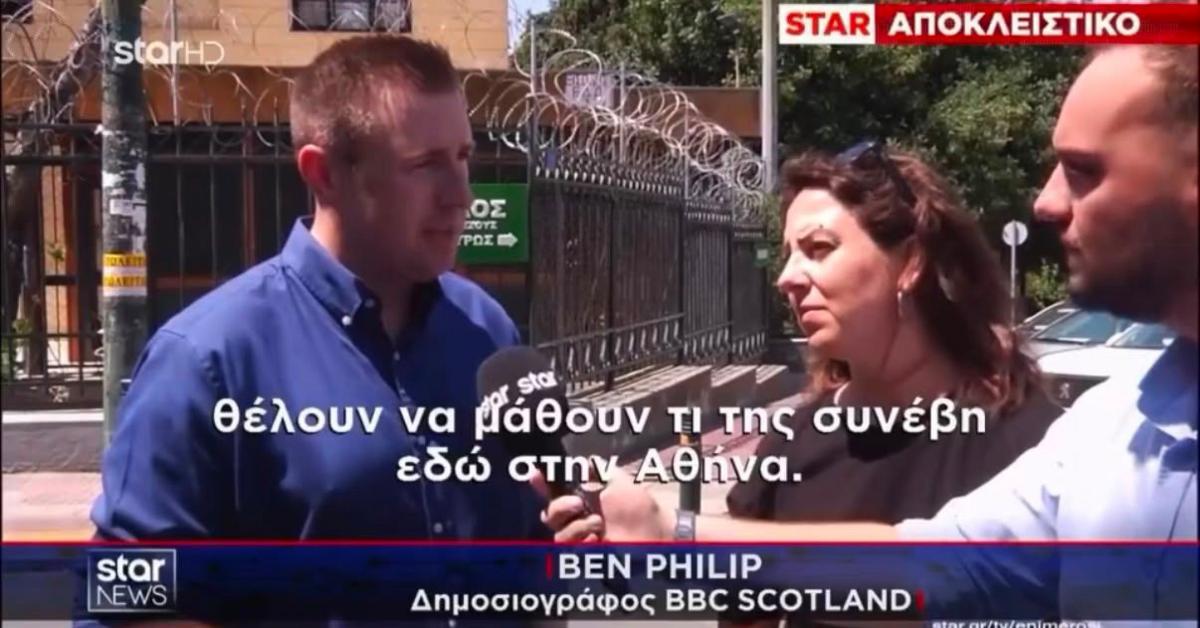 Television news screenshot showing an outdoor interview beside a metal security fence topped with razor wire. Three people are visible in the foreground, with one person speaking into a microphone while another holds recording equipment. Greek-language captions appear across the screen, along with a news banner and the text "STAR ΑΠΟΚΛΕΙΣΤΙΚΟ" at the top. Trees, fencing, and a building are visible in the background.