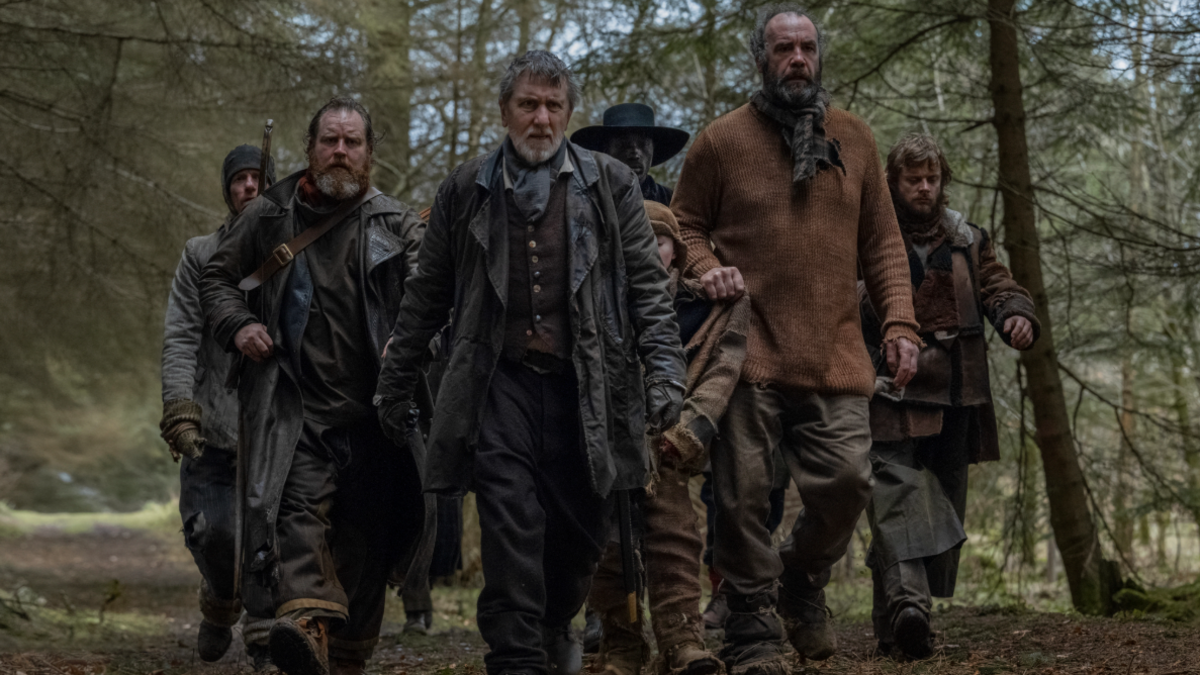 A group of men wearing wild west clothing walking through a forest