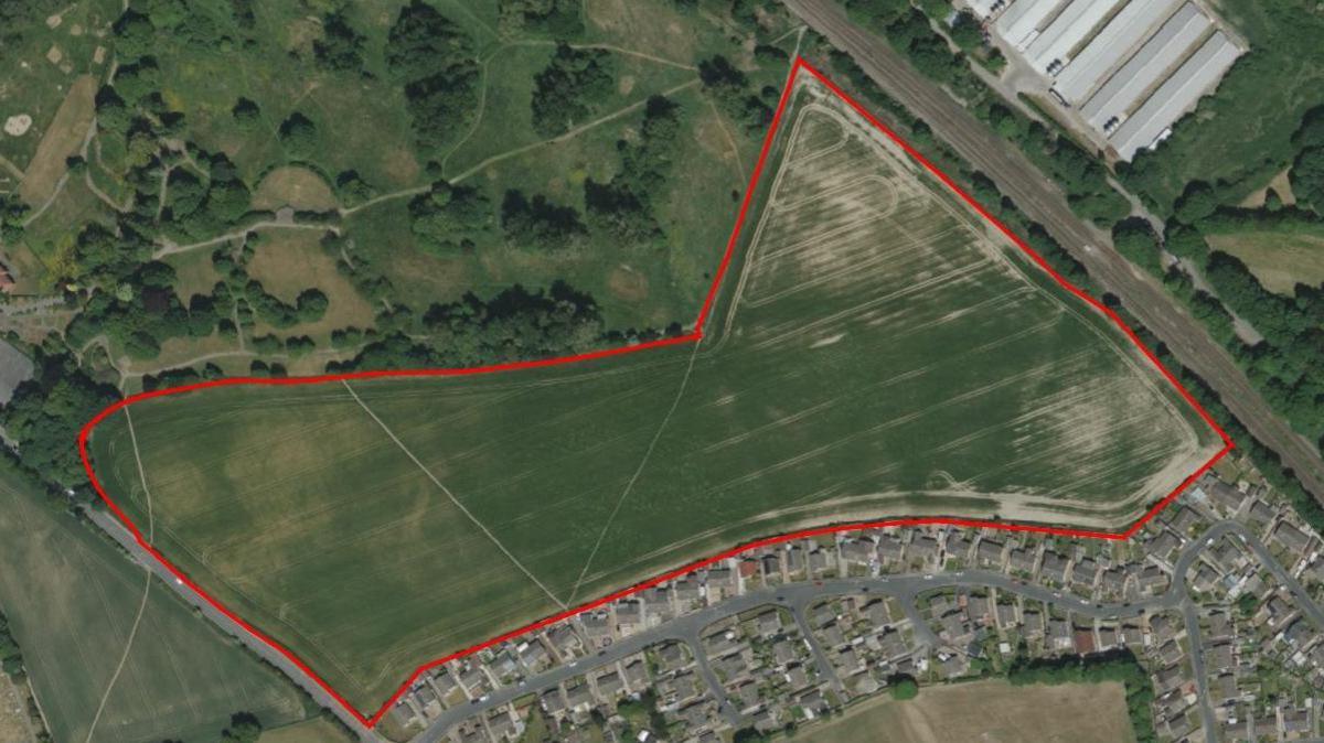 A map showing the red outline of the green farmland where the homes would be built, with existing houses to the south.