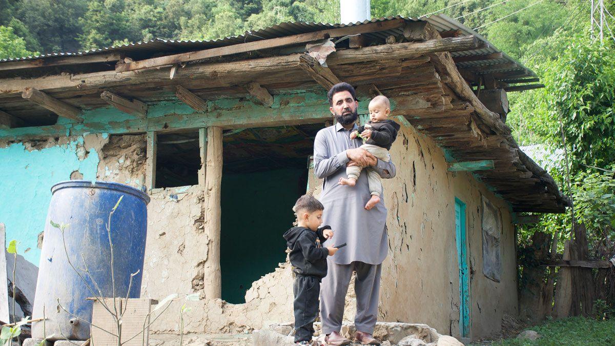 Muhammed stands with his two young children in front of his bombed home