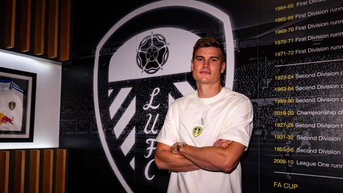 Jaka Bijol stands in front of Leeds badge after signing