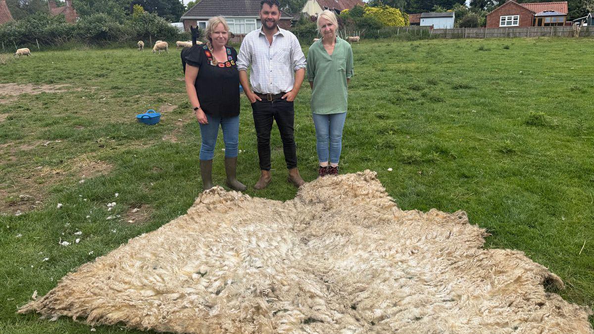 Two women and one man stand behind the fleece which is stretched out over the grass.