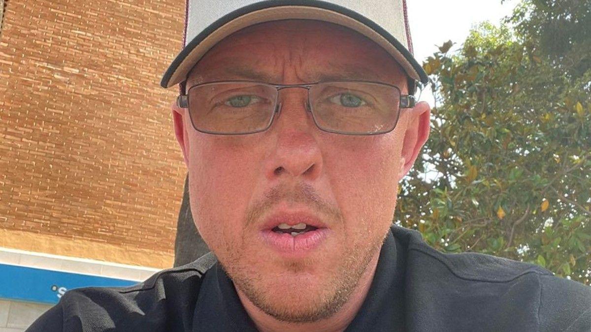 Matthew White, a young man wearing rectangular glasses, a dark shirt and a white baseball cap, looks into the camera close up.