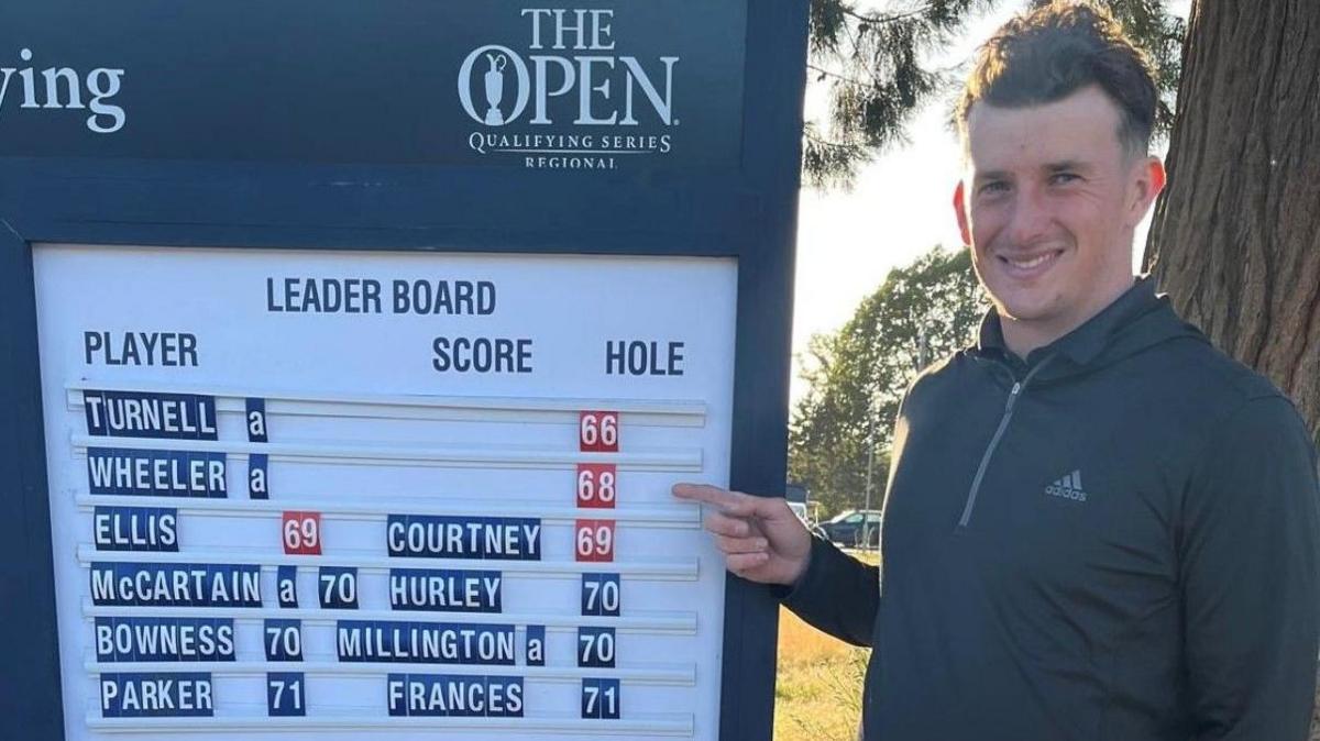 Rob Wheeler poses for a photo while pointing at the leaderboard at the regional qualifying for The Open Championship