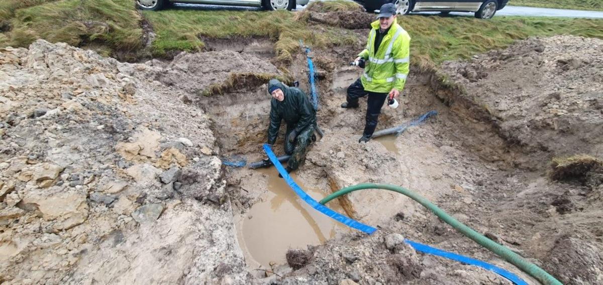 Two men installing cabes in a muddy, water-filled hole