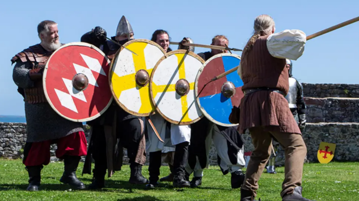 A wide of six people dressed in medieval clothing holding shields and spears.