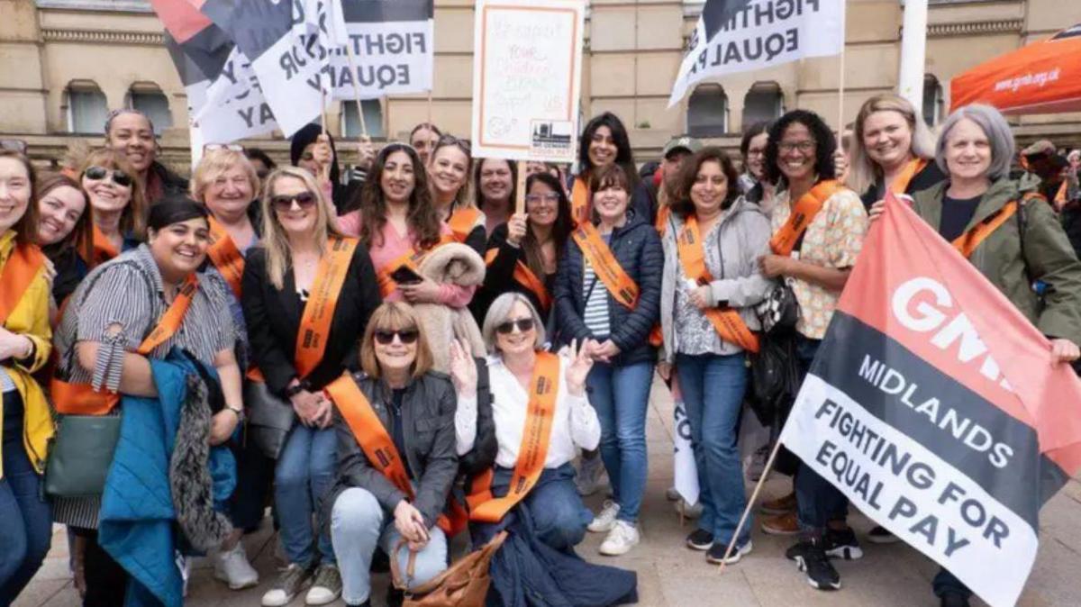 A large group of women with placards and flags, wearing orange sashes