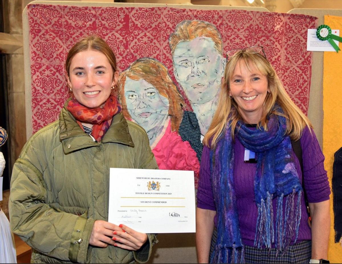 Shrewsbury College student Cecily Penrice standing on the left smiling and holding a certificate and Moreton Hall textile teacher Vickie Owen smiling on the right. Behind them is Cecily's huge portrait made of fabric of a couple an their adopted child