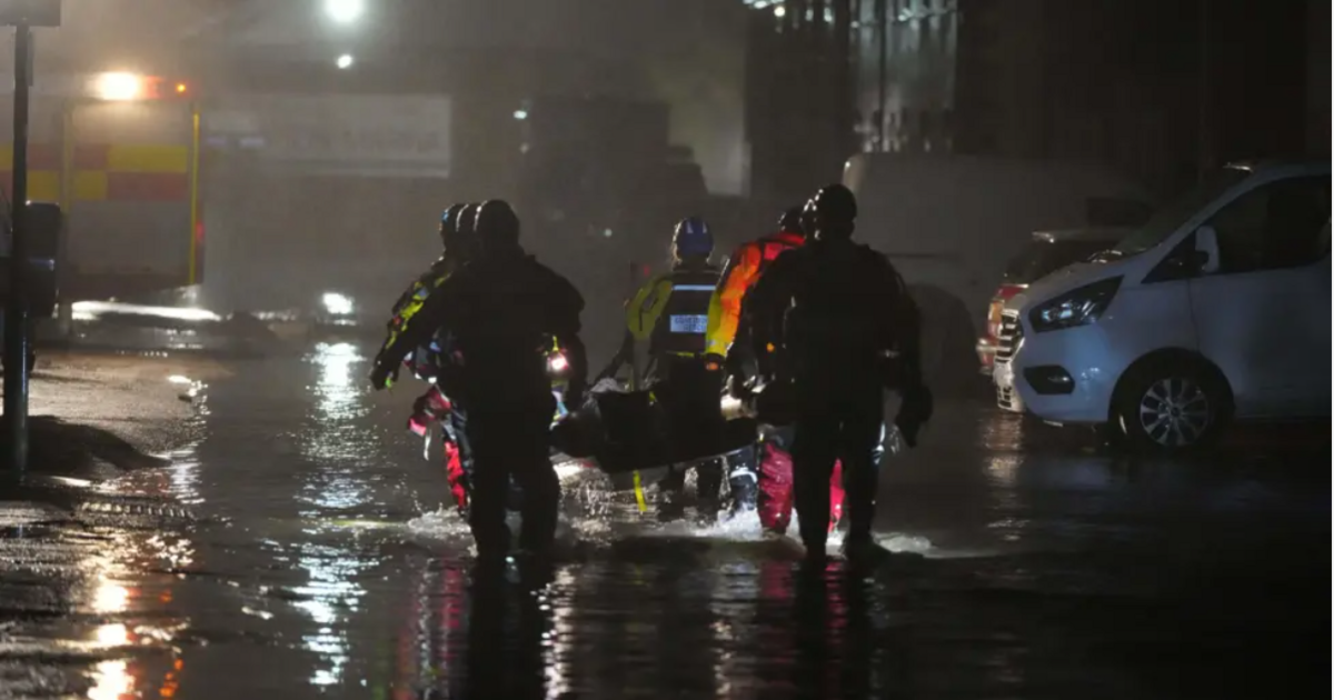 Emergency service personnel walking through flood water in the dark carrying a stretcher