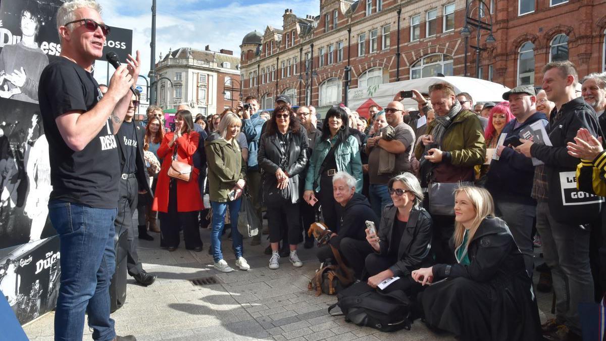 A crowd of people watch a speech at the unveiling of the plaque in Leeds