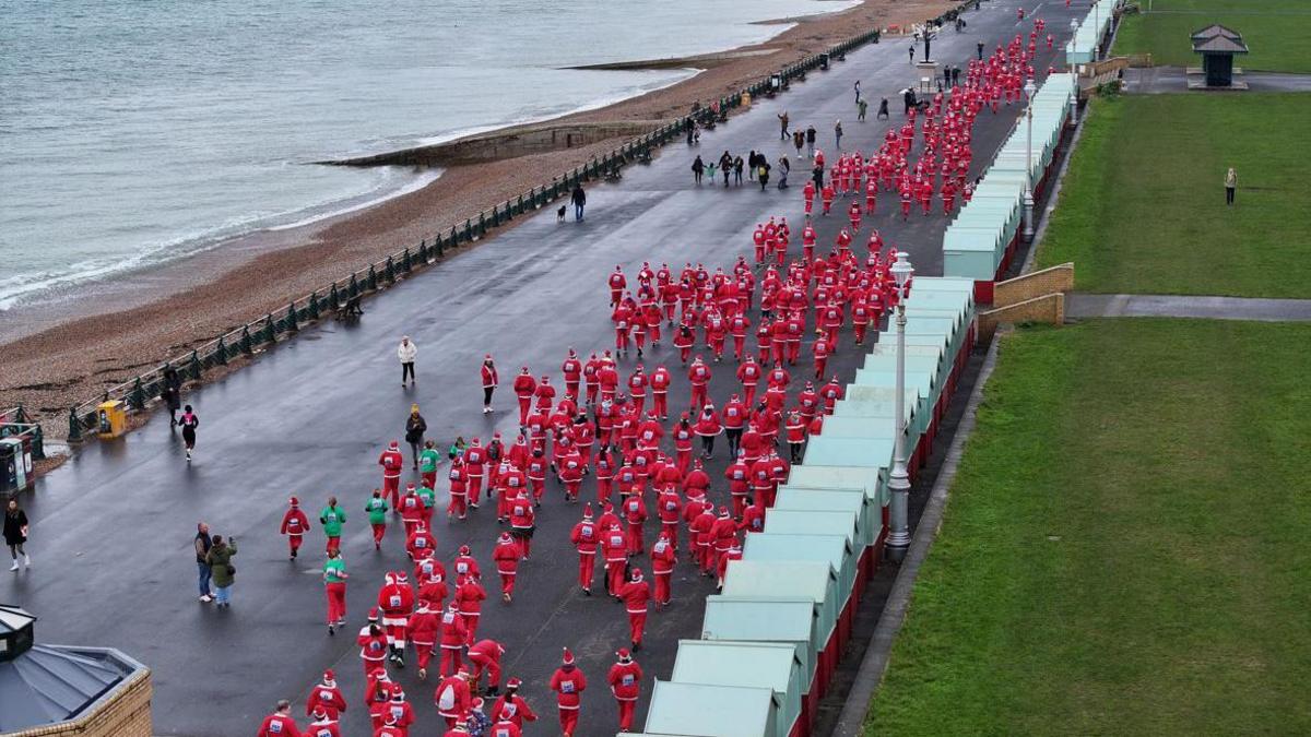 A drone shot of hundreds of people running on Hove seafront, next to the beach on one site and beach huts on the other. All are wearing red and white outfits, a white beard and a Christmas hat.