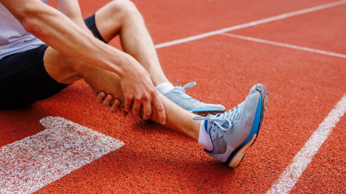 Athlete holding his leg injured after running at track and field stadium after jogging, running competition, sports injury concept