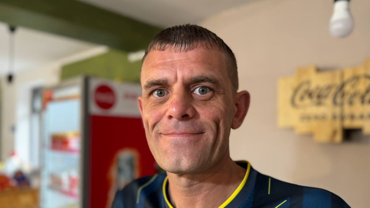 A man smiles at the camera. He has short dark hair with a fringe and wears a sports top.