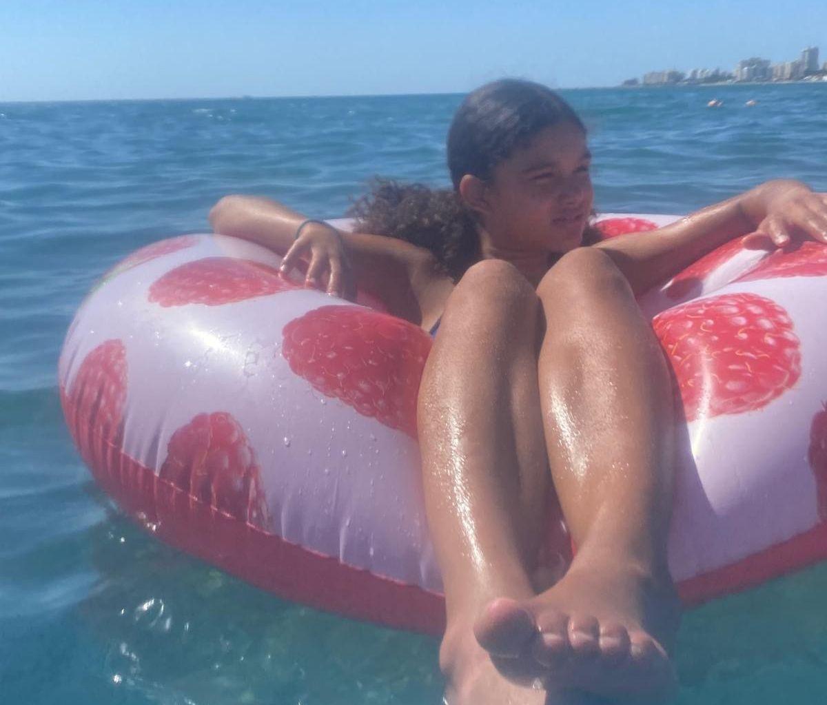 Mia is sitting in her swimsuit on an inflatable pink beach float in the sea in the summer time.