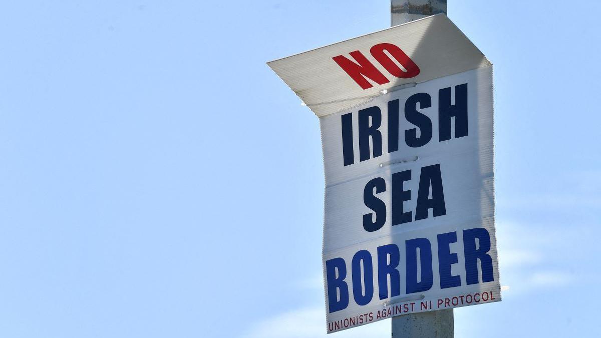 A white poster on a street light saying 'No Irish Sea Border' in coloured writing. The sky behind the sign is blue.