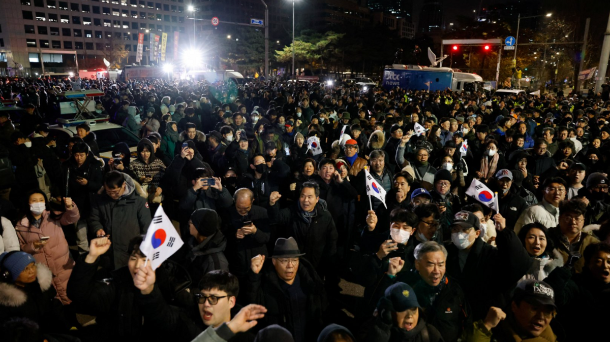 A crowd of protesters outside parliament chant 'No Martial law' and hold up the South Korean flag.