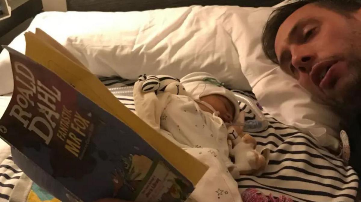 Ryan Lock, laying beside his baby daughter Ida in bed, reading a Roald Dahl's Fantastic Mr Fox.