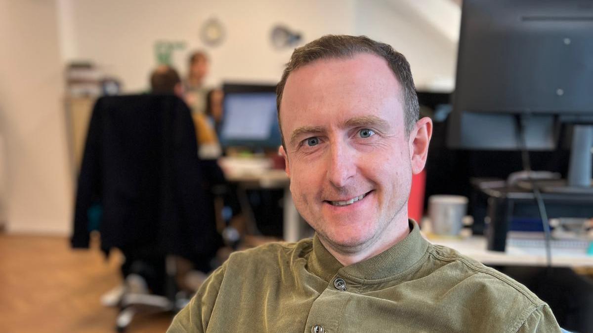 CEO Mick Ross has short brown hair and is smiling at the camera. He is sitting in an office.